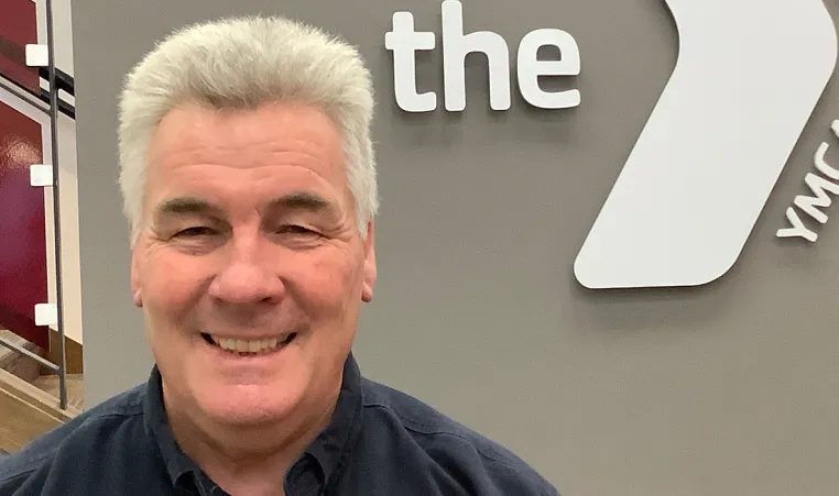 man with grey hair smiling in front of a ymca