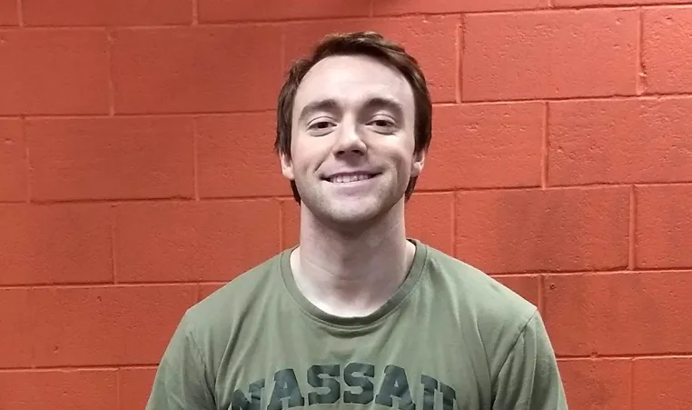 young man smiling at the camera against an orange wall