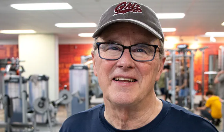 a man with a baseball hat and glasses smiling in an indoor weight lifting gym