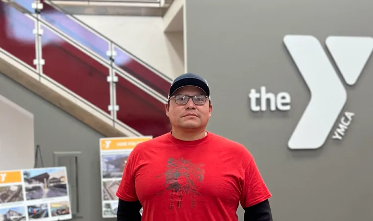 Man in red shirt with glasses standing in front of Y logo 