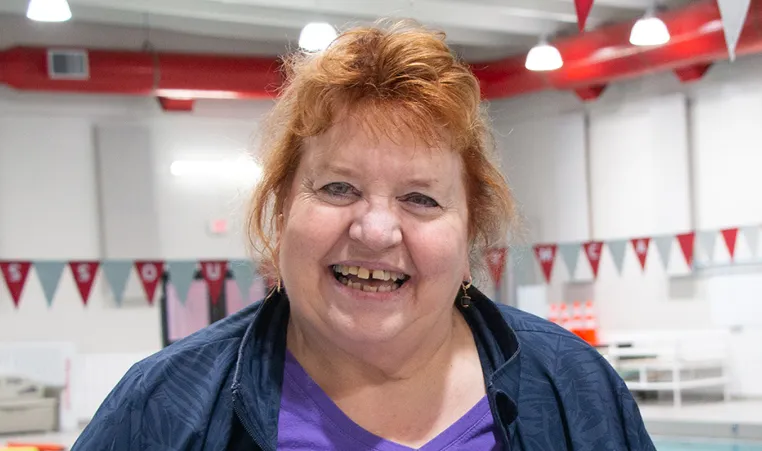 women with red hair and a blue jacket and purple shirt smiles at the camera