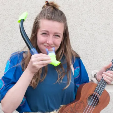 a young woman with long brown hair and a blue shirt holding a snorkle and a ukelele