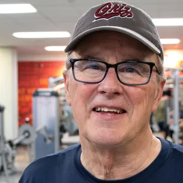 a man with a baseball hat and glasses smiling in an indoor weight lifting gym