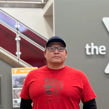 Man in red shirt with glasses standing in front of Y logo 