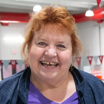 women with red hair and a blue jacket and purple shirt smiles at the camera