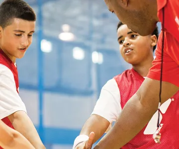 children in basketball jerseys and their coach putting their hands together for a cheer