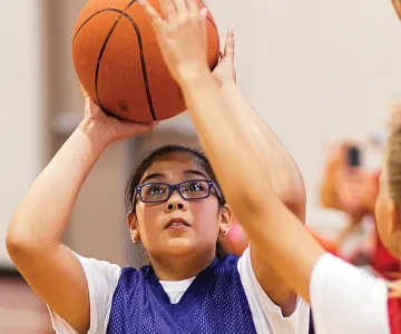 a child preparing to throw a basketball; another child blocking them