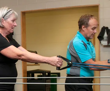 two older adults in fitness clothes using stretching bands at a gym