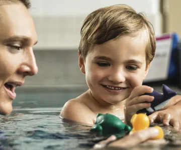 young swimmer and a swim instructor playing with toys in a pool