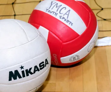 two volleyballs sitting on a gym floor next to a volleyball net laying on the gorund