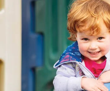 a smiling young child with curly red hair goes down a playground slide