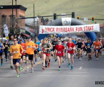 a large group of runners take off from the start line of a race in a city's downtown