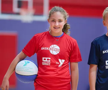 two preteens in basketball jerseys holding basketballs